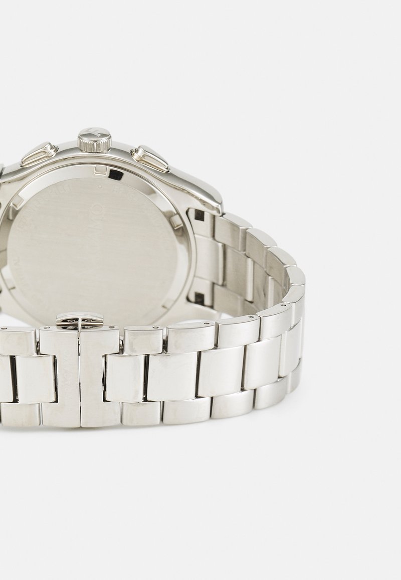 Ceas de mână din metal argintiu, cu un design elegant, având o brățară din oțel inoxidabil strălucitor și două butoane laterale pe carcasă.