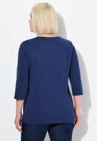 Top blu navy a tre quarti in tessuto morbido. Presenta un collo rotondo e una vestibilità rilassata, con un orlo posteriore leggermente più lungo.