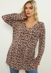 Långärmad blommig tunika med V-ringning, i en kr�ämfärgad grund med röda och bruna blommönster. Mjuk, texturerad tyg med en avslappnad passform.