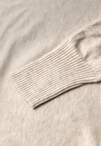 Helle beigefarbene Strickpullover mit geripptem Bündchen und weicher Textur, einem glatten Stoffkörper und subtilen Farbvariationen.