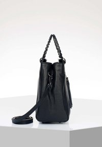 Sac à main en cuir texturé noir avec poignées tressées et bandoulière amovible, posé debout sur une surface blanche.