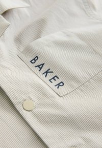 Beige gestreiftes Hemd mit einer Brusttasche, auf der "BAKER" steht. Verfügt über einen Knopfdetail und einen strukturierten Stoff für zusätzlichen visuellen Reiz.