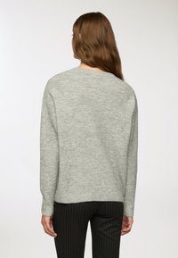 Maglione grigio a maglia con scollo rotondo e maniche lunghe. Presenta una vestibilità rilassata e polsini a costine. Texture liscia, dettagli minimali.