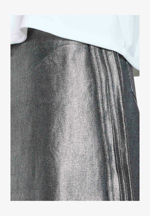 Gonna argento metallico con strisce verticali cucite vicino all'orlo, abbinata a una maglia bianca semplice.