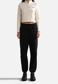 Top corto de forro polar crema con cuello alto y cremallera en el cuello. Joggers negros ajustados con cintura elástica. Calzado negro completa el conjunto.