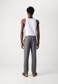 Gray linen pants with an elastic waistband and two back pockets, paired with a white tank top and black sandals, viewed from the back.