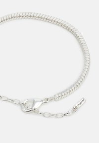 Silver-tone metal chain bracelet featuring a flexible, flat design with a clasp closure and a short extension chain with a logo tag.