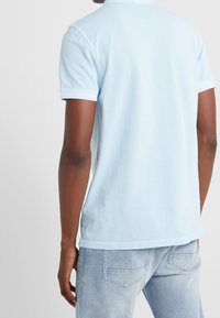 Světle modré bavlněné tričko s krátkým rukávem, žebrovaným límečkem a volným střihem, doplněné o světle modré džíny.