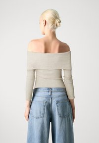 Beige ribbet off-shoulder topp med lange, tettsittende ermer, sammen med høyt liv lyseblå baggy jeans. Strukturert stoff er synlig.