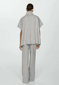 Un haut gris ample de style poncho avec un col montant, associé à un pantalon large assorti en tissu doux et texturé.