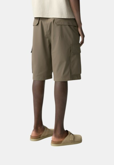 Pantaloni cargo beige, caratterizzati da due tasche laterali e una vestibilità comoda. Indossati con scarpe slip-on in beige chiaro. Tessuto sintetico liscio.
