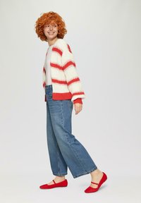 Gebreide cardigan in crème met rode strepen, gecombineerd met hoge, loszittende blauwe jeans en rode flats met een band over de voet.