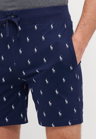 Shorts de bain navy avec des motifs de petits joueurs de polo blancs, taille élastique avec cordon de serrage et poches latérales. Texture de tissu douce.