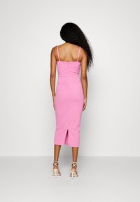 Roze aansluitende jurk met dunne schouderbandjes, halflang, met een rits aan de achterkant en een split aan de zoom. Glad materiaal. Minimale details.