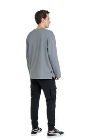 Gray long-sleeve shirt with a relaxed fit, paired with black cargo pants featuring side pockets and ribbed cuffs, worn with black sneakers.