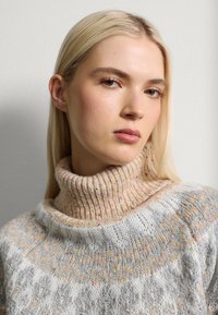 Strickpullover mit hohem Rippkragen; in Grau- und Cremetönen mit einem gesprenkelten Muster und weicher Textur.