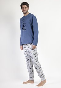 Camiseta azul de manga larga con estampado de dibujos animados en negro, combinada con pantalones de pijama grises que presentan personajes de dibujos animados multicolores. Ajuste suave y relajado.