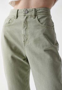 Světle zelené džíny s vysokým pasem vyrobené z bavlněné směsi, se pěti kapsami, předním zapínáním na knoflík a diskrétními švy.