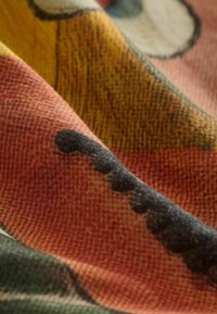 Gros plan d’un tissu plié avec un imprimé visage de dessin animé coloré comprenant les couleurs rouge, jaune, noir et rose.