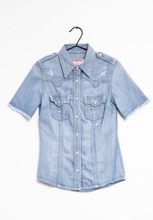 Lichtblauw korte mouw denim overhemd met knopen aan de voorkant, twee borstflapzakken, rafelige mouwzomen en schouderepauletten aan een zwarte hanger.