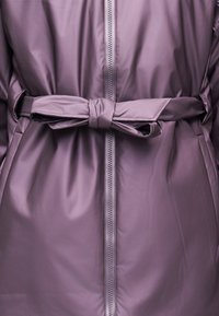 Μωβ παλτό με φερμουάρ στο μπροστινό μέρος και ταιριαστό ζώνη δεμένο σε φιόγκο στη μέση, λεία υφή, κοντινό πλάνο στη μέση.