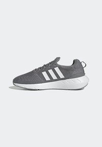 Gray athletic sneaker with white sole and three white stripes on the side, featuring a lace-up design and pull tab at the heel.