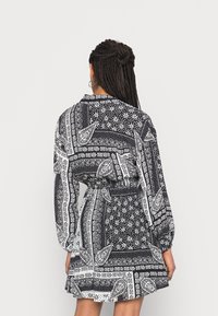 Vestido em preto e branco com padrão, mangas longas, cintura ajustada e barra com babados; apresenta desenhos em paisley e florais.