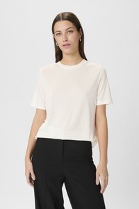 Cremefarvet t-shirt med korte ærmer og rund hals, i blød tekstur, parret med sorte bukser. Enkel design, ingen synlige mønstre eller accenter.