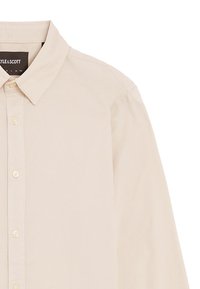Lys beige skjorte med knapper lavet af bomuld. Har klassisk krave, lange ærmer og forreste placket med små knapper. Glat tekstur.