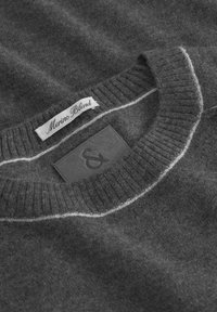 Dunkelgrauer Merinowolle-Pullover mit geripptem Kragen und weißen Nähten, mit eingenähten Etiketten, darunter "Merino Blend."