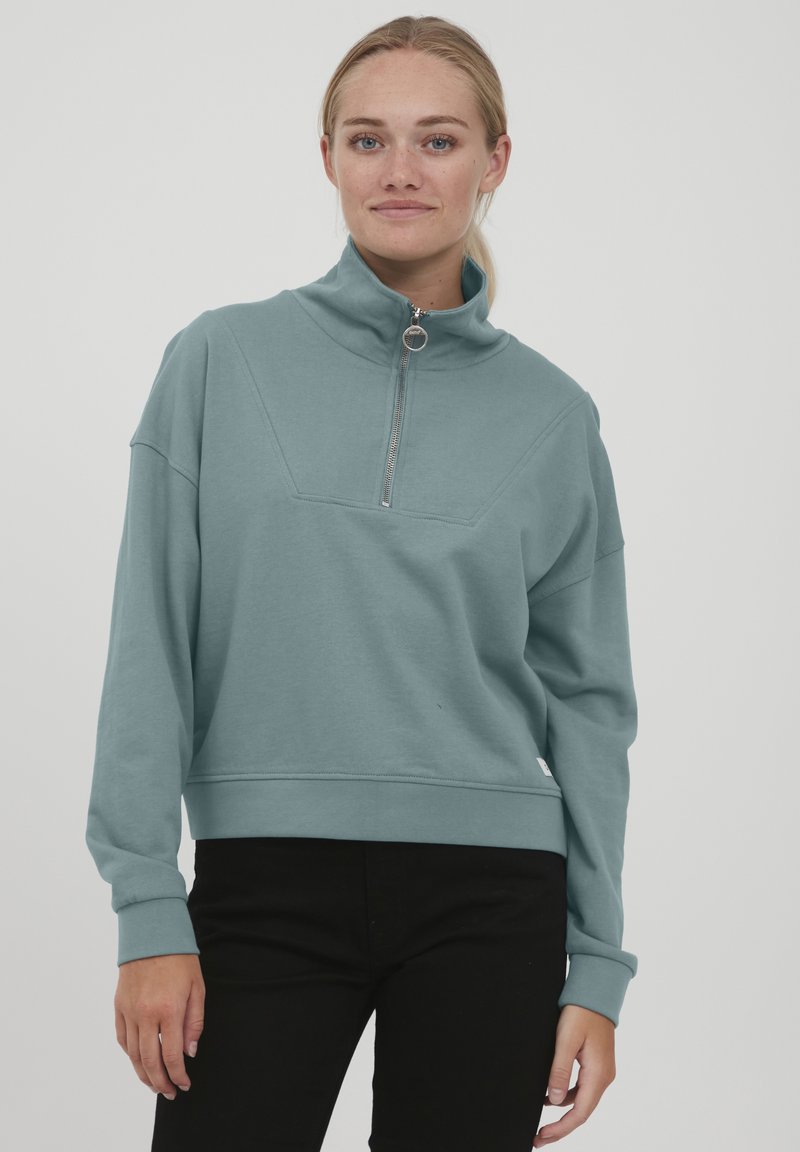Ljusblå sweatshirt med hög krage, fjärdedel dragkedja och ribbat avslut. Har en geometrisk paneldesign och långa ärmar. Tillverkad i bomullsblandning.