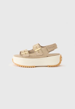 Beige suede platform sandal with two adjustable buckle straps, a back strap, thick white sole, and textured gum rubber outsole.