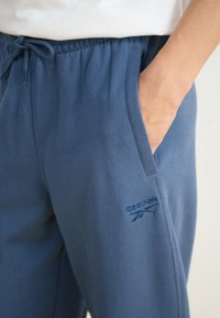 Jogging en coton bleu avec une taille élastique, un cordon de serrage et des poches latérales. Présente un logo Reebok brodé sur la cuisse gauche.