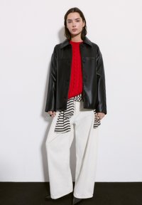 Czarna skórzana kurtka z przodem na guziki, czerwony sweter w warkocze, szerokie białe spodnie z paskiem w paski oraz czarne buty na spiczastym nosku.