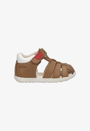 Bruine leren sandaal met een witte hak en een rood logo. Heeft een open teen, meerdere riempjes en een flexibele rubberen zool.