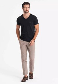 Czarna bawełniana koszulka z dekoltem w serek, dopasowane beżowe spodnie, brązowe buty, minimalne akcenty, gładka tekstura, nowoczesny casualowy design.