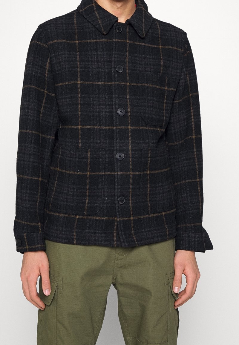 Czarna i brązowa koszula w kratę, wykonana z teksturowanej tkaniny, z przodem zapinanym na guziki, dużym kołnierzem i bocznymi kieszeniami.