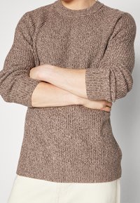 Sweter dziany w ciepłym odcieniu brązu, z prążkowanym wykończeniem, okrągłym dekoltem i rękawami o długości trzech czwartych. Prosta, dopasowana linia.