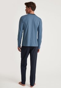 Langarmige blauwe top met een zwarte halslijn, gecombineerd met donkerblauwe broek. De stof lijkt zacht en lichtgewicht, ontworpen voor comfort.
