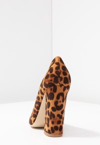 Hnědé lodičky s leopardím vzorem, texturovaný svršek připomínající nubuk, špičatá špička a masivní podpatek, s výraznými černými skvrnami na tanovém pozadí.