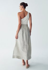 Asymmetrical white ribbed top paired with a light gray linen maxi skirt featuring an elastic waistband and side slits, viewed from behind.