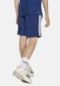 Shorts atléticos azul marino con rayas laterales blancas, hechos de una tela ligera. Llevados con calcetines blancos y zapatos grises con detalles negros.