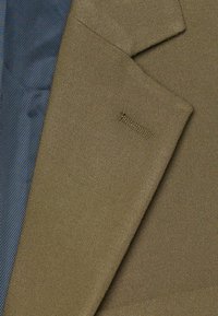 Blazer in tessuto testurizzato verde oliva con fodera a righe blu scuro. Presenta rever a punta e un logo del marchio visibile ricamato sulla tasca.