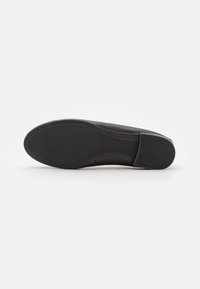 Semelle de chaussure en caoutchouc noir avec une texture lisse et une forme légèrement courbée. Présente des rainures horizontales pour la traction et un design à bout arrondi.