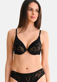 Soutien-gorge en dentelle noire avec un décolleté plongeant et des bonnets moulés. Dispose de bretelles ajustables et d'un accent doré au centre. Texture lisse.