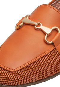 Oranje leren schoen met een gestructureerd mesh onderstuk en een decoratieve gesp in goudkleur. Gladde afwerking met contrasterende materialen.