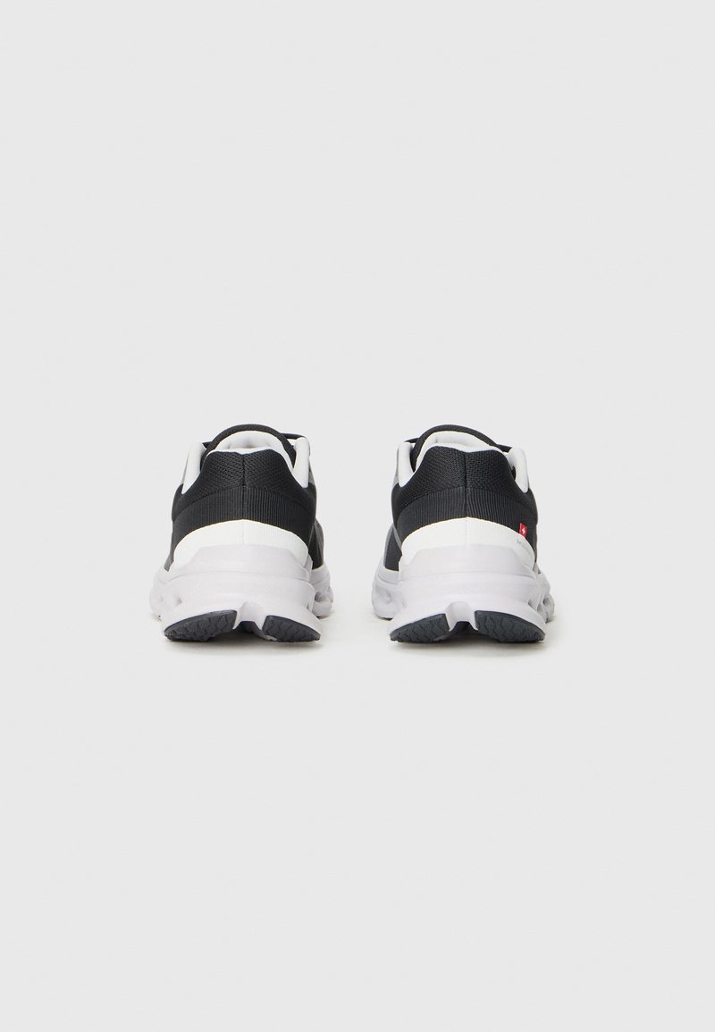 Schwarz-weiße Sportschuhe mit einem strukturierten Mesh-Obermaterial, gepolsterter Sohle und markantem Gummiprofil, von hinten betrachtet.