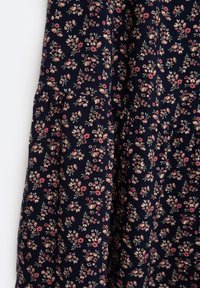 Marineblomstret kjole med et blødt, tekstureret stof. Har små pink og grønne blomster, lagdelt design og diskrete volanger langs sømmene.
