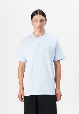 Camiseta de algodón de color azul claro con mangas cortas, cuello redondo y un pequeño logo de Nike en una tonalidad más oscura en el pecho. Textura suave.