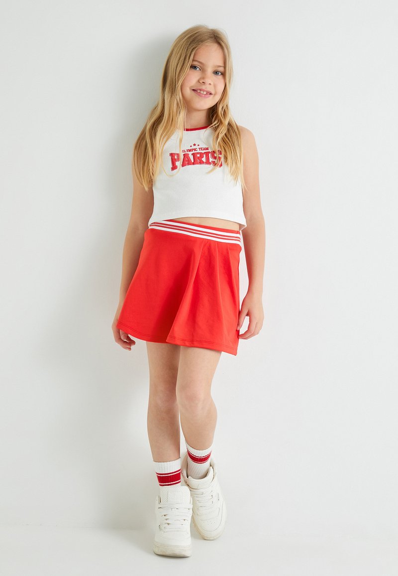 Hvid crop top med rød tekst, rød flagrende nederdel med stribet talje, parret med hvide sneakers og røde stribede sokker.